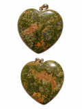 Two heart-shaped polished stone pendants with gold-tone loops, displayed vertically on a plain white background. The stones have a mottled pattern of olive green, orange, and brown.